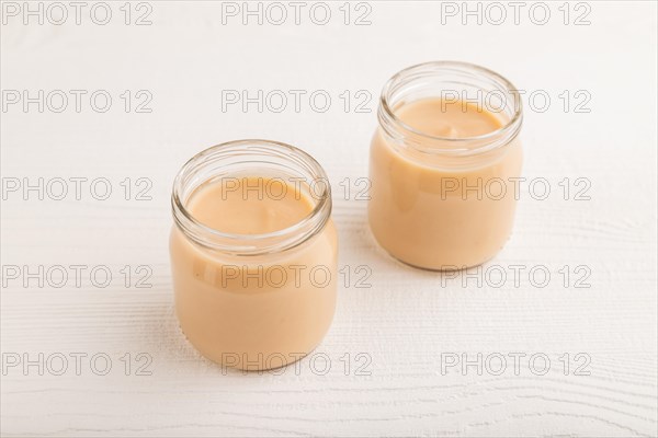 Baby puree with fruits mix, apple, banana infant formula in glass jar on white wooden background.
