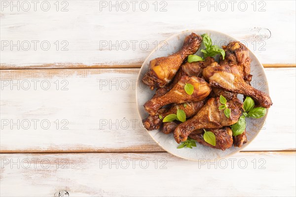 Smoked chicken legs with herbs and spices on a ceramic plate on a white wooden background. Top