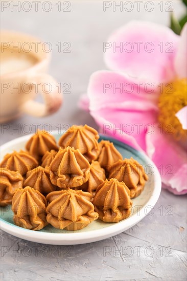 Homemade soft caramel fudge candies on blue plate and cup of coffee on gray concrete background,