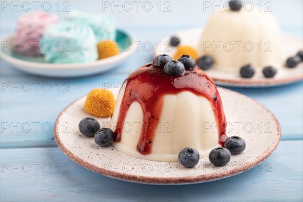 White milk jelly with blueberry jam on blue wooden background and blue linen textile. side view,