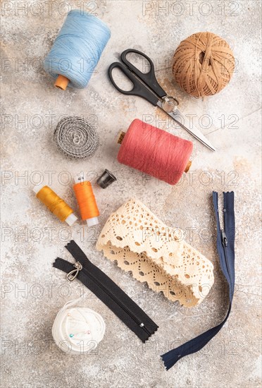 Sewing accessories: scissors, thread, thimbles, braid on brown concrete background. Top view, flat