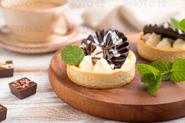 Sweet tartlets with chocolate and cheese cream with cup of coffee on a white wooden background and