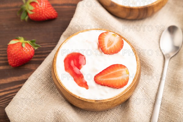 Grained cottage cheese with strawberry jam on brown wooden background and linen textile. side view,