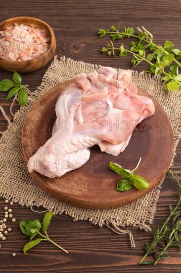 Raw turkey wing with herbs and spices on a wooden cutting board on a brown wooden background and
