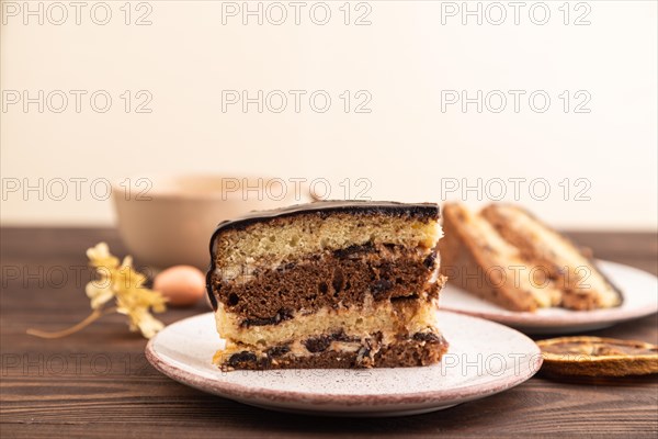 Chocolate biscuit cake with caramel cream, cup of coffee on brown wooden background. side view,