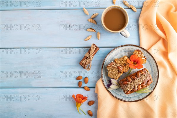 Caramel and almond cake with cup of coffee on blue wooden background and orange linen textile. top