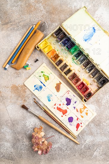 Drawing accessories set: brushes, pencils, watercolor on brown concrete background. Top view, flat