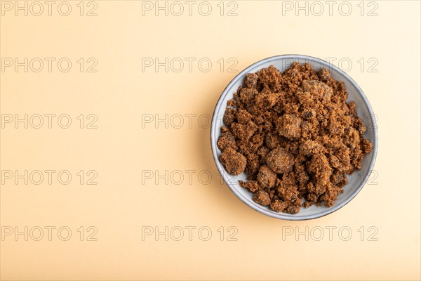 Plate with unrefined brown cane sugar on orange pastel background. top view, flat lay, copy space