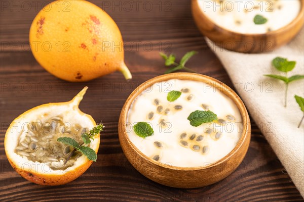 Yoghurt with granadilla and mint in wooden bowl on brown wooden background and linen textile. side