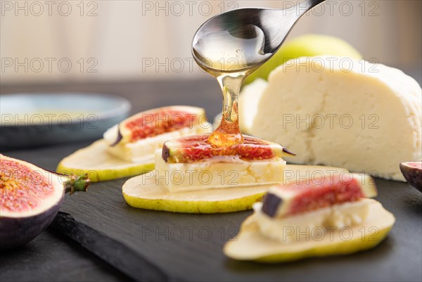 Summer appetizer with pear, cottage cheese, figs and honey on slate board on a black concrete
