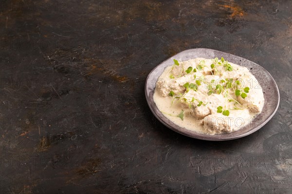Stewed chicken fillets with coconut milk sauce and rucola microgreen on black concrete background.