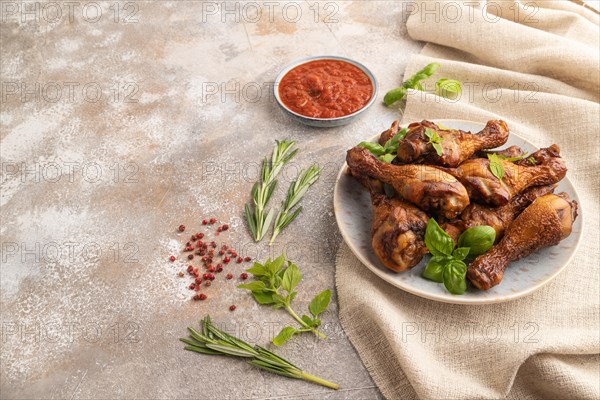 Smoked chicken legs with herbs and spices on a ceramic plate with linen textile on a brown concrete