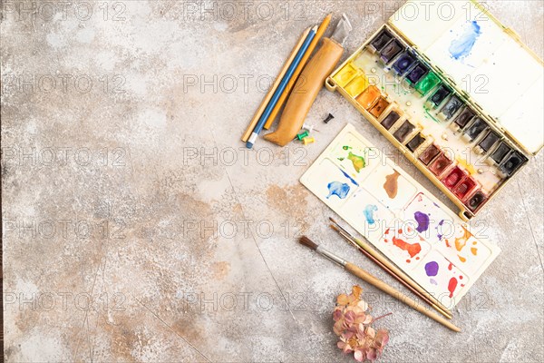 Drawing accessories set: brushes, pencils, watercolor on brown concrete background. Top view, flat
