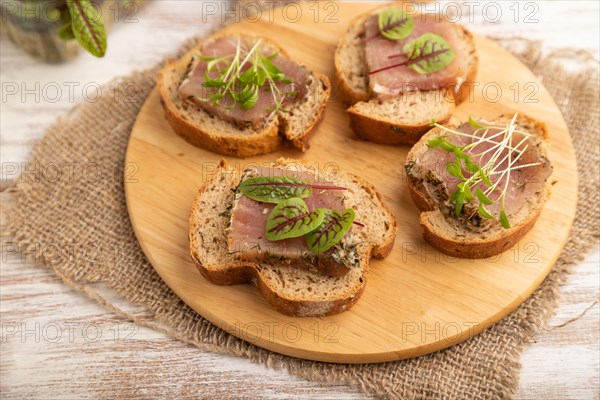 Bread sandwiches with jerky salted meat, sorrel and cilantro microgreen on white wooden background