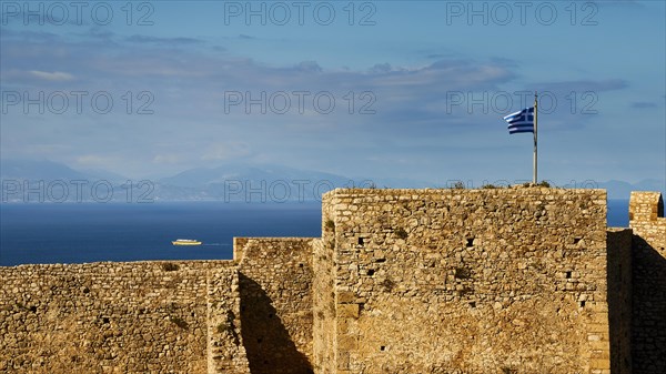 Historic fortress walls under a partly cloudy sky with Greek flag and sea view, Chlemoutsi, High