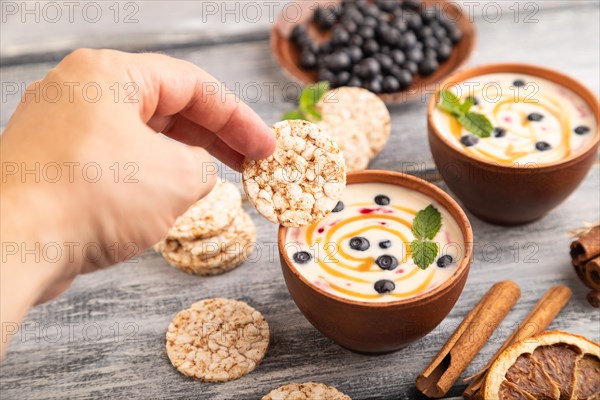 Yoghurt with bilberry and caramel in clay bowl on gray wooden, hand dipping cookies in yogurt, side