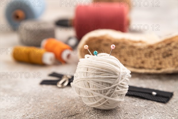 Sewing accessories: scissors, thread, thimbles, braid on brown concrete background. Side view,