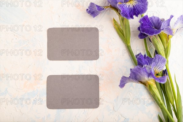 Gray business card with blue iris flowers on white concrete background. top view, flat lay, copy