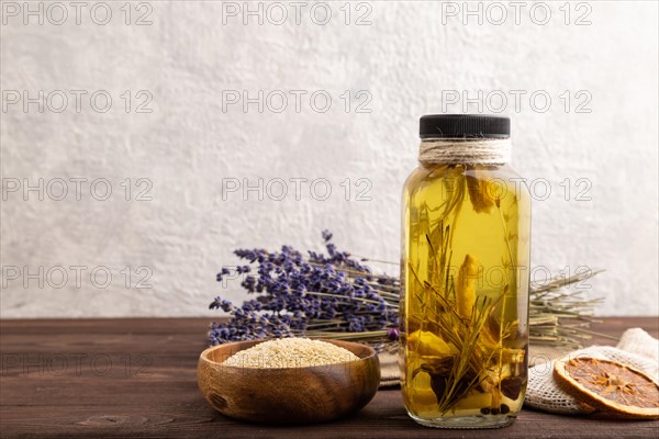 Sunflower oil in a glass jar with various herbs and spices, lavender, sesame, rosemary on a brown
