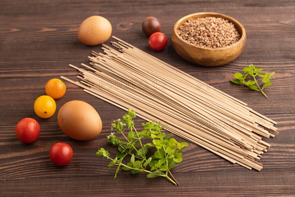 Japanese buckwheat soba noodles with tomato, eggs, spices, herbs on brown wooden background. Side