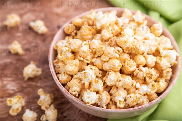 Popcorn with caramel in ceramic bowl on brown concrete background and green textile. Side view,