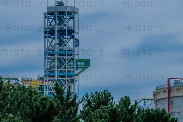 Platform tower at a gasoline storage facility on a cloudy day with pine trees in the foreground