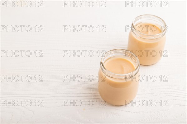Baby puree with fruits mix, apple, banana infant formula in glass jar on white wooden background.