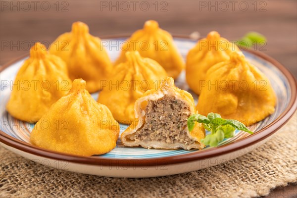 Fried manti dumplings with pepper, basil on brown wooden background and linen textile. Side view,