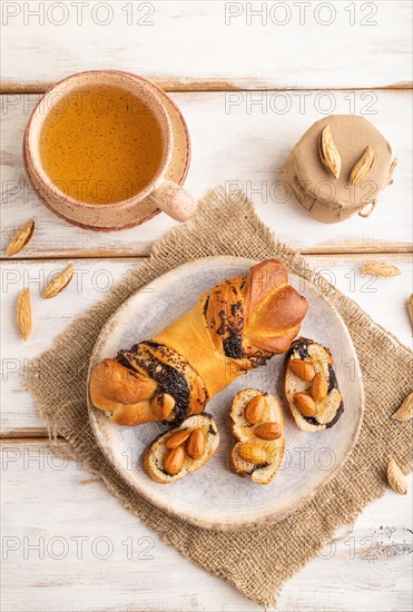 Homemade sweet bun with honey almonds and cup of green tea on a white wooden background and linen
