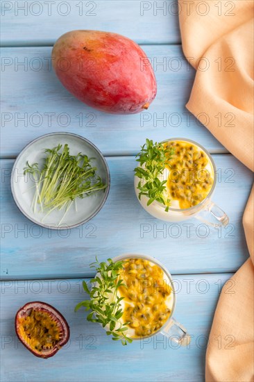 Mango yogurt with passionfruit and cilantro microgreen in glass on blue wooden background with