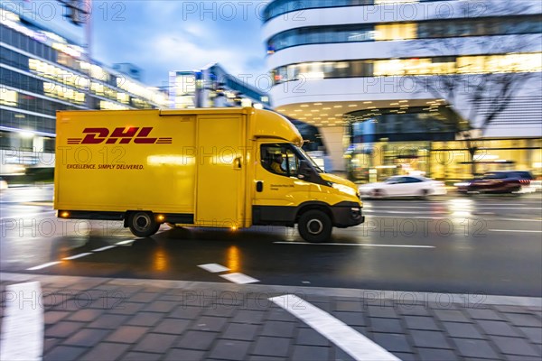 Vehicle of the parcel service provider DHL, modern architecture of the city centre in the evening,