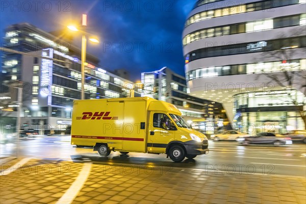 Vehicle of the parcel service provider DHL, modern architecture in the evening, motion blur,