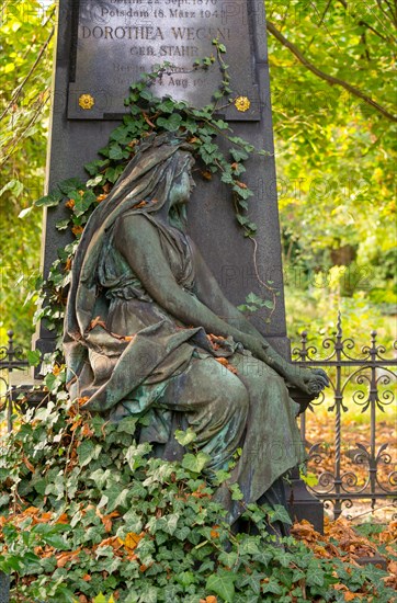 Detail of a green patinated cemetery sculpture surrounded by ivy and trees, autumn leaves,