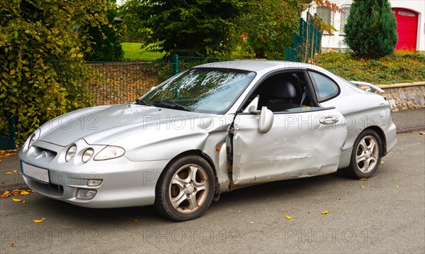 Accident car, sporty car with accident damage standing on a road, silver motor vehicle, car with