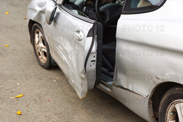 Accident car, sporty car with accident damage standing on a road, damaged, open door, silver motor