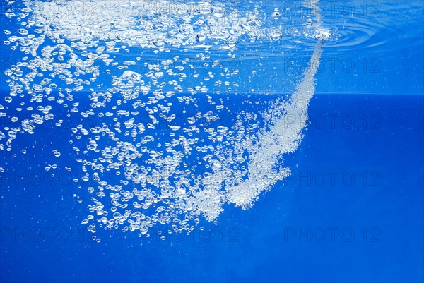 A thin jet of water penetrates the water surface and produces many air bubbles in the blue water of