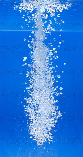 A thin jet of water penetrates the water surface and produces many air bubbles in the blue water of