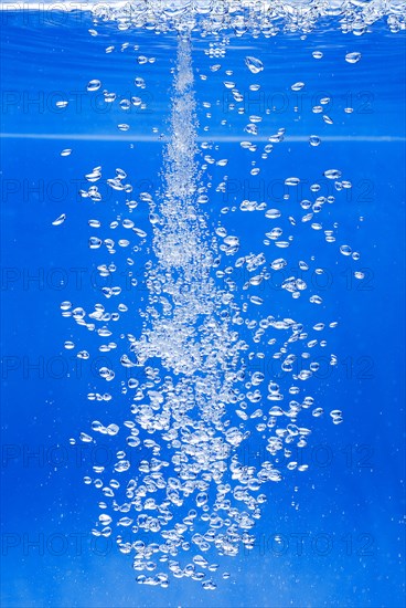 A thin jet of water penetrates the water surface and produces many air bubbles in the blue water of