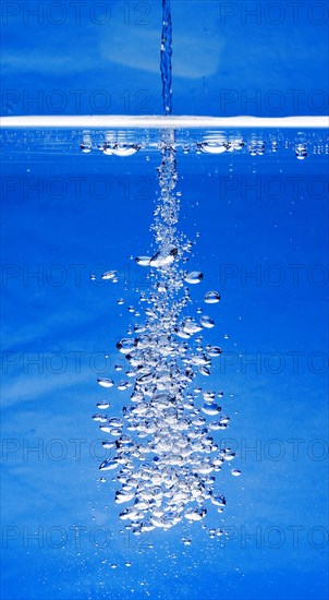A thin jet of water penetrates the water surface and produces many air bubbles in the blue water of