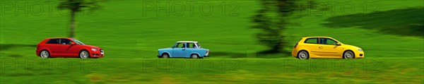 A red and a yellow car drive quickly through the green meadow landscape, a Trabant, also known as a