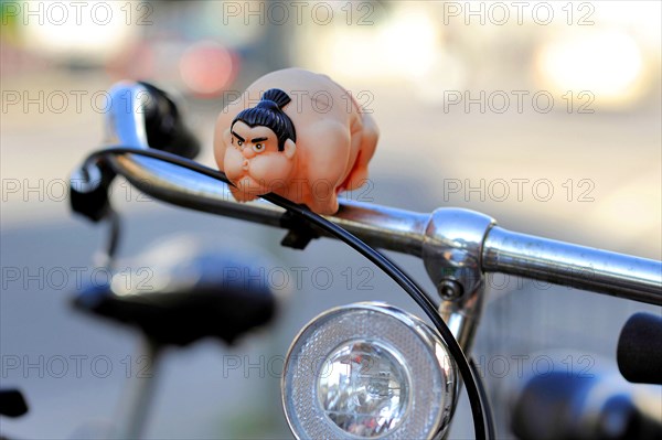 A sumo wrestler attached to the handlebars of a bicycle as a bicycle horn or bell