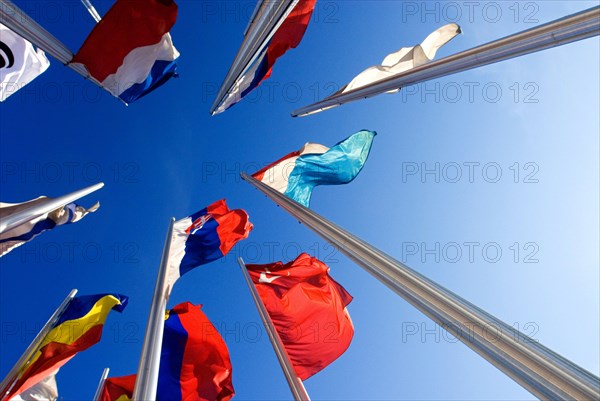 Wide angle shot of European national flags, frog perspective, against blue sky, in front of the