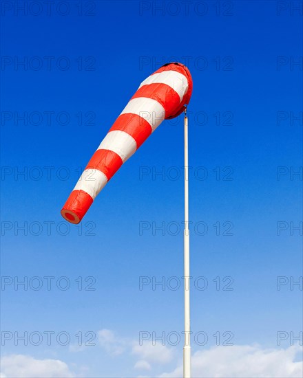 A red and white windsock blows in a light breeze against a blue sky