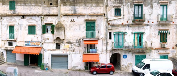 old dilapidated facade of a residential building with balconies and a used car dealer in Minori,
