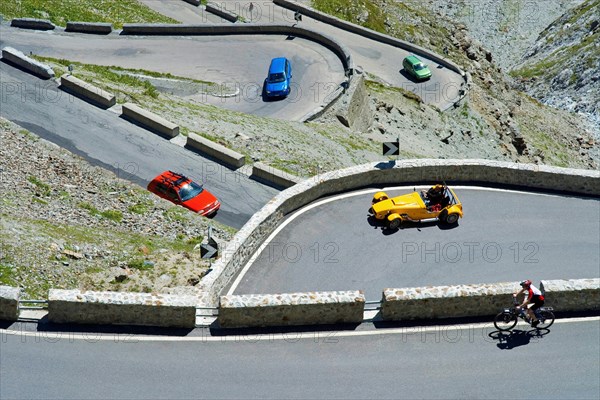 A red, green and blue car, a yellow roadster and a bicycle driver in hairpin curves on the Stelvio