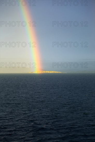 Seascape view of spectrum colours in rainbow over sea and island, Norway, Europe