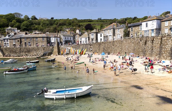 People on crowded beach in Mousehole village, Cornwall, England, UK
