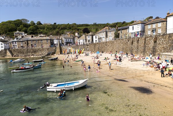 People on crowded beach in Mousehole village, Cornwall, England, UK