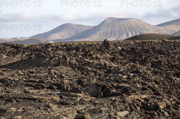 Volcanic landscape of solidified lava flows and distant cone volcanoes, near Yaiza, Lanzarote,