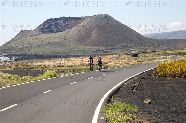 Cyclists on road leading to cone of Mount Corona volcano and Ye village, Haria, Lanzarote, Canary